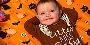Starr joined the competition — help win amazing prizes! baby, black_cat, brown_clothing, child, colorful_toy, crib, cute, face, halloween_theme, happy, indoor, infant, lying_down, onesie, orange_sheet, person, pumpkin, skull, smile, toy