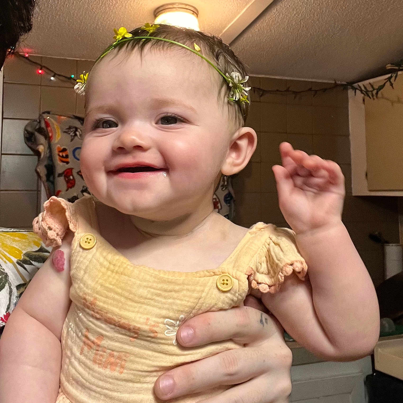 Starr is registered to the contest to win money with this photo: apparel, baby, button, child, cute, dressed, face, flower_crown, hand, happy, headwear, holding, indoor, infant, kitchen, light, person, skin, smiling, warm_lighting