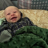 Koda joined the competition — help win amazing prizes! baby, infant, child, smiling, happy, face, portrait, indoor, blanket, green_blanket, plaid_clothing, cushion, couch, seated, lying_down, cozy, home, patterned_background, photography, joy