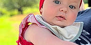 Elizabeth is registered to the contest to win money with this photo: baby, cheek, child, closeup, curious, dress, face, greenery, hand, headband, headwear, holding, outdoor, person, portrait, red_clothing, shoulder, soft_light, star_pattern, summer