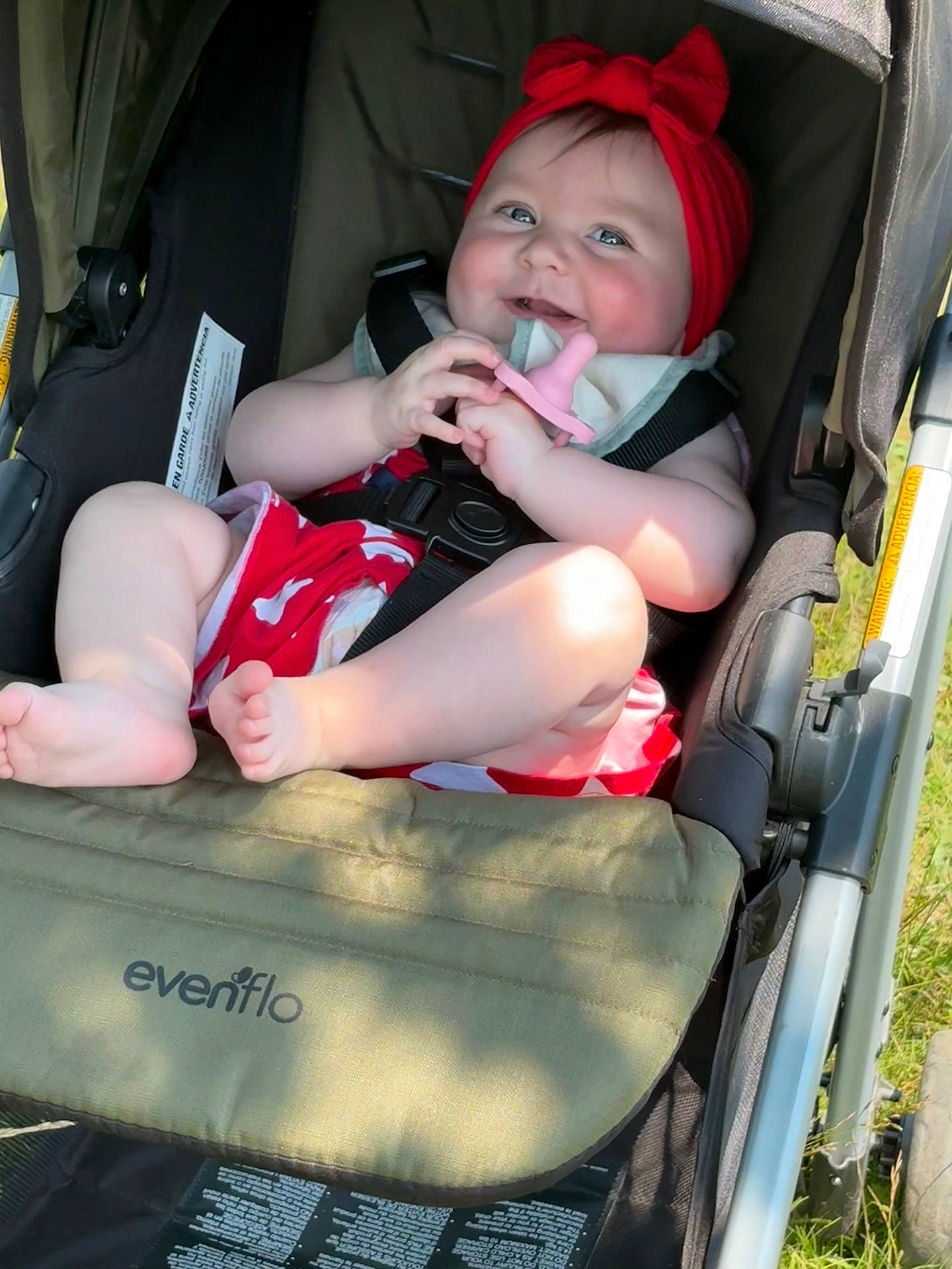 baby, cheeks, child, clothing, cute, feet, grass, happy, infant, legs, outdoor, pacifier, person, portrait, red_headband, seatbelt, smiling, stroller, summer, sunlight