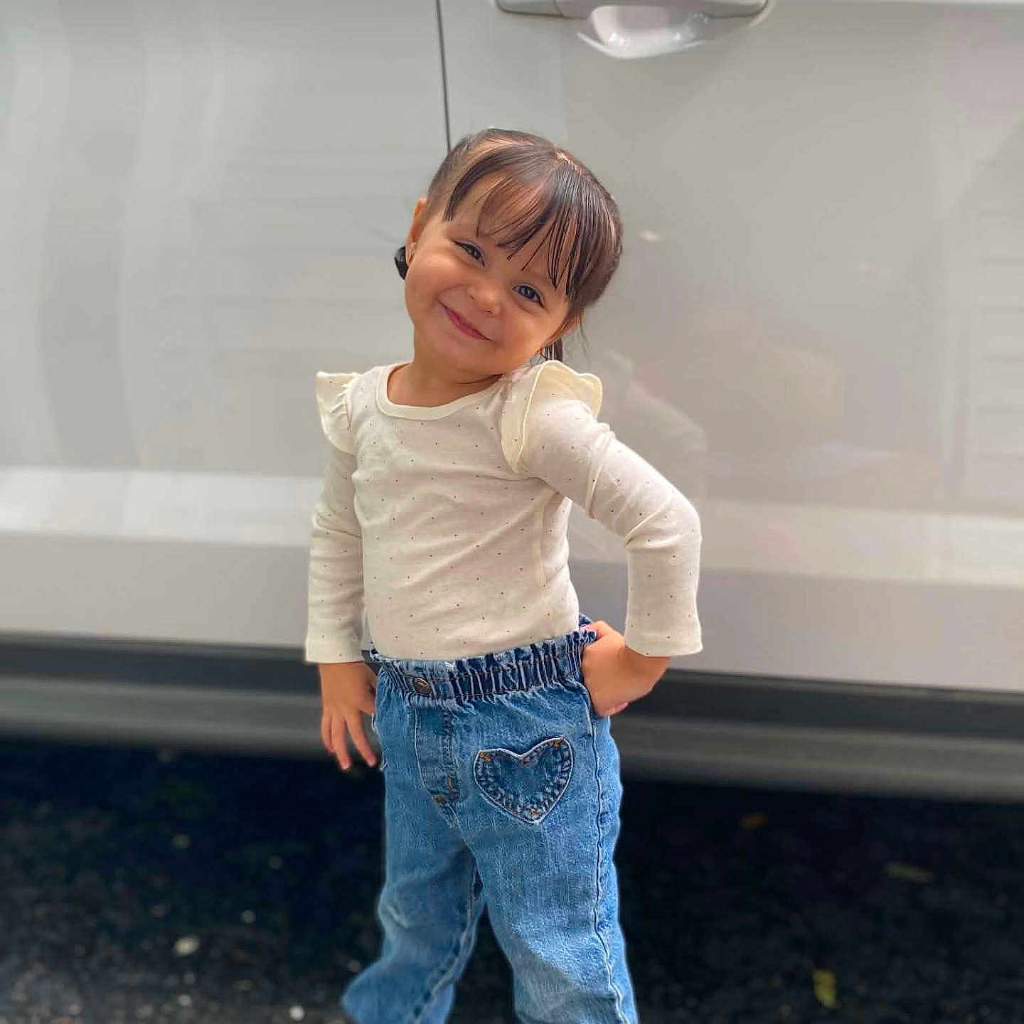 Eliza Arevalo is registered to the contest to win money with this photo: car, child, daylight, denim, fashion, girl, heart_pocket, jeans, long_sleeves, outdoor, portrait, posing, road, shirt, shoes, smiling, standing, toddler, vehicle, white_car