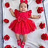 baby, child, infant, portrait, lying_down, red_dress, polka_dots, hair_bow, matching_shoes, roses, flowers, floral_arrangement, white_blanket, baby_bed, indoor, top_down, fashion, cute, face, photography
