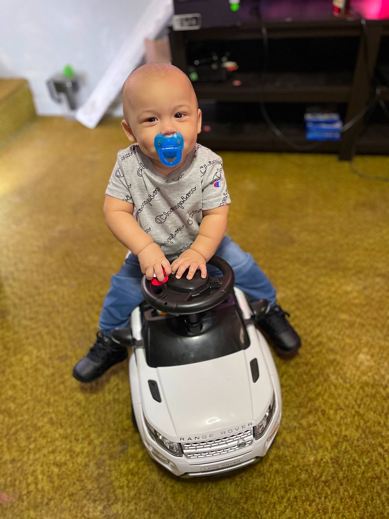 Jasani is registered to the contest to win money with this photo: automotive_design, automotive_exterior, automotive_lighting, automotive_tire, automotive_wheel_system, bumper, car, floor, flooring, headlamp, hood, jeans, motor_vehicle, person, personal_luxury_car, riding_toy, shoe, sneakers, toddler, trousers