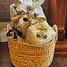 basket, brick_wall, calico_cat, cat, container, cozy, curious, decor, decoration, festive, flower, gift, holiday, indoor, ornament, pet, plant, white_flower, wood_floor, wrapped_gifts