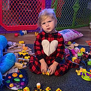 Aarika is registered to the contest to win money with this photo: child, toddler, pajamas, heart_pattern, rubber_ducks, toys, carpet, playpen, wooden_blocks, stuffed_toys, floor, indoor, yellow, red, black, plush, person, sitting, playroom, expression