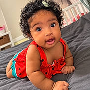 Olivia joined the competition — help win amazing prizes! baby, child, infant, portrait, curly_hair, wide_eyed, surprised, smiling, red_outfit, watermelon_pattern, hair_clip, bedroom, bed, blanket, bedding, indoors, photography, sitting, crawling, cute