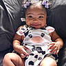 Olivia is registered to the contest to win money with this photo: baby, child, infant, smiling, portrait, curly_hair, hair_bows, cow_print, onesie, outdoorless, seated, chair, black_background, happy, cute, face, hands, legs, fashion, photography
