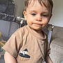 toddler, child, indoor, beige_tshirt, bird_graphic, playpen, blanket, blue_eyes, short_hair, curious, soft_texture, furniture, home, person, casual_clothing, young_child, expression, portrait, standing, daylight
