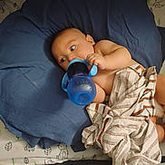 Landen joined the competition — help win amazing prizes! baby, child, blue_cup, cushion, striped_cloth, bed, pillow, indoor, person, infant, bottle, blanket, resting, cute, lying_down, nursery, soft_fabric, comfort, feeding, young