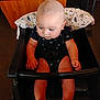 arms, baby, bald_head, carpet, child, clothing, cute, expression, face, floor, furniture, high_chair, indoor, infant, legs, onesie, person, pillow, seat, wood