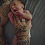 newborn, baby, tattoo, hand, ring, bracelet, skin, diaper, person, expression, holding, fingers, arm, tattooed_arm, jewelry, bed, fabric, closeup, portrait, indoor