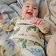 Landen is registered to the contest to win money with this photo: baby, dinosaur_pajamas, smiling, lying_down, bed, blanket, pillow, infant, happy, child, cozy, cute, person, home, sleepwear, soft_fabric, morning, indoors, portrait, playful