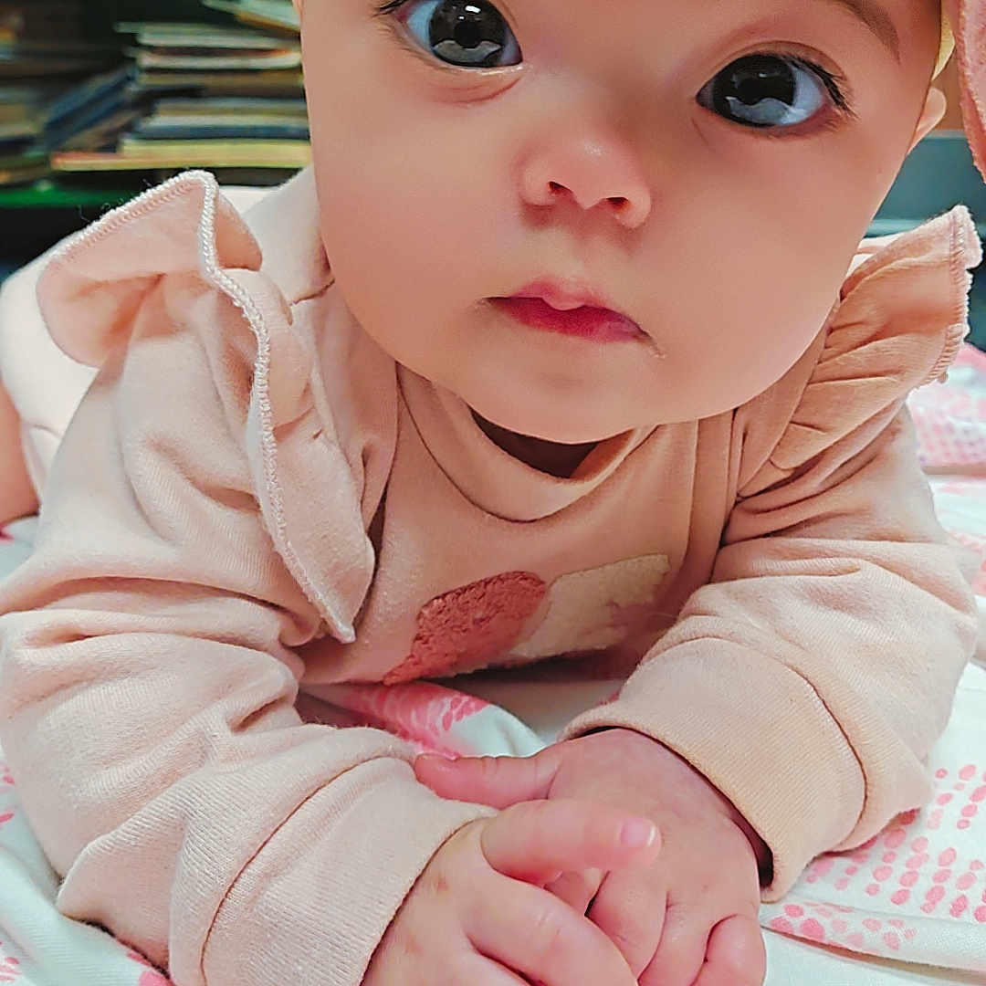 Oliviah is registered to the contest to win money with this photo: baby, blanket, bookshelf, bow, child, close_up, curious_eyes, cute, face, hands, headband, indoor, infant, laying_down, patterned_blanket, pink_clothing, portrait, soft_fabric, warm_lighting, young_child