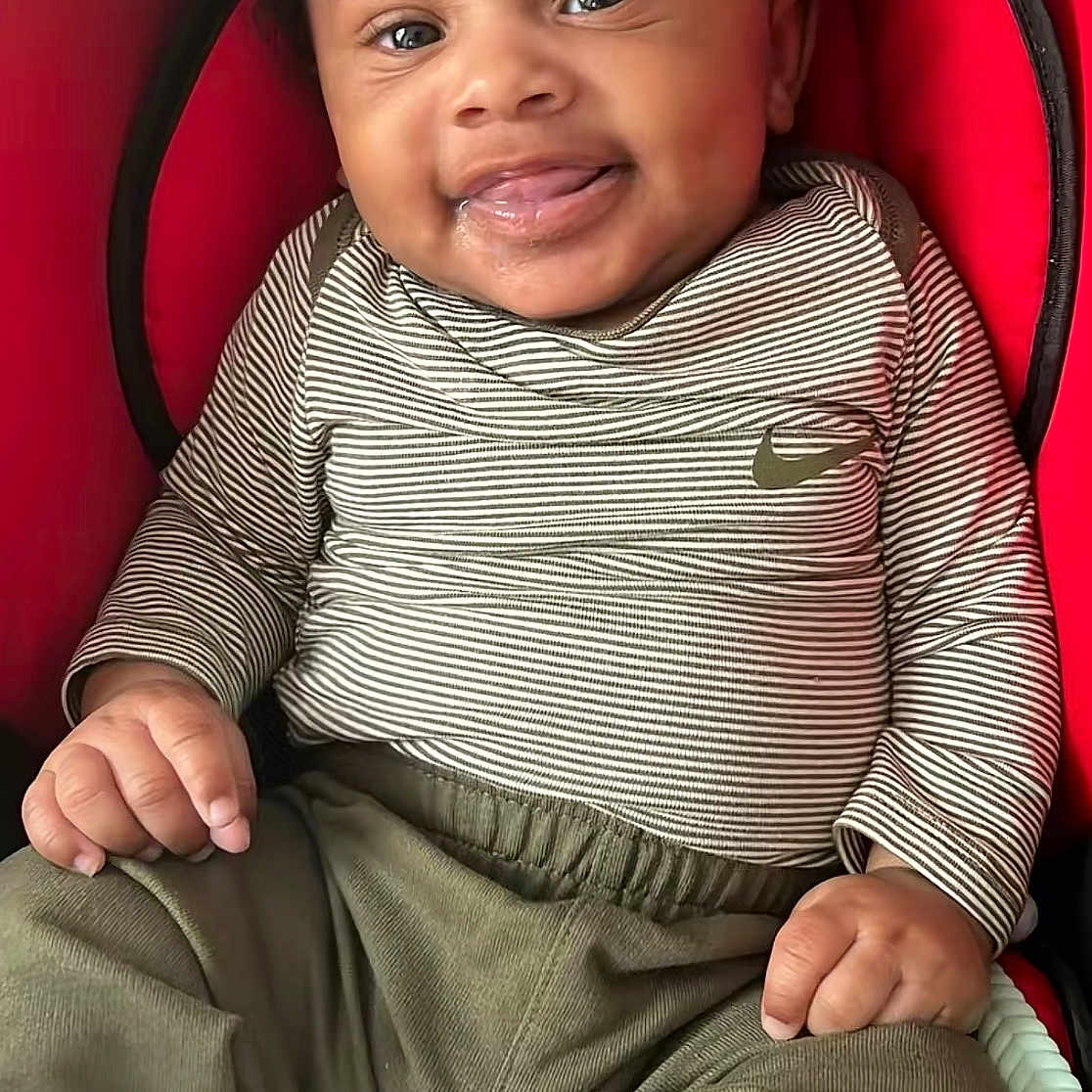 Dawson is registered to the contest to win money with this photo: baby, child, smiling, striped_shirt, green_pants, car_seat, indoor, cute, happy, infant, sitting, clothing, young_child, portrait, person, baby_clothes, expression, tongue_out, head, hands