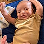 baby, smile, arms_up, onesie, blanket, cushion, infant, happy, lying_down, foot, hand, face, skin, head, child, newborn, cozy, indoors, comfort, relaxed