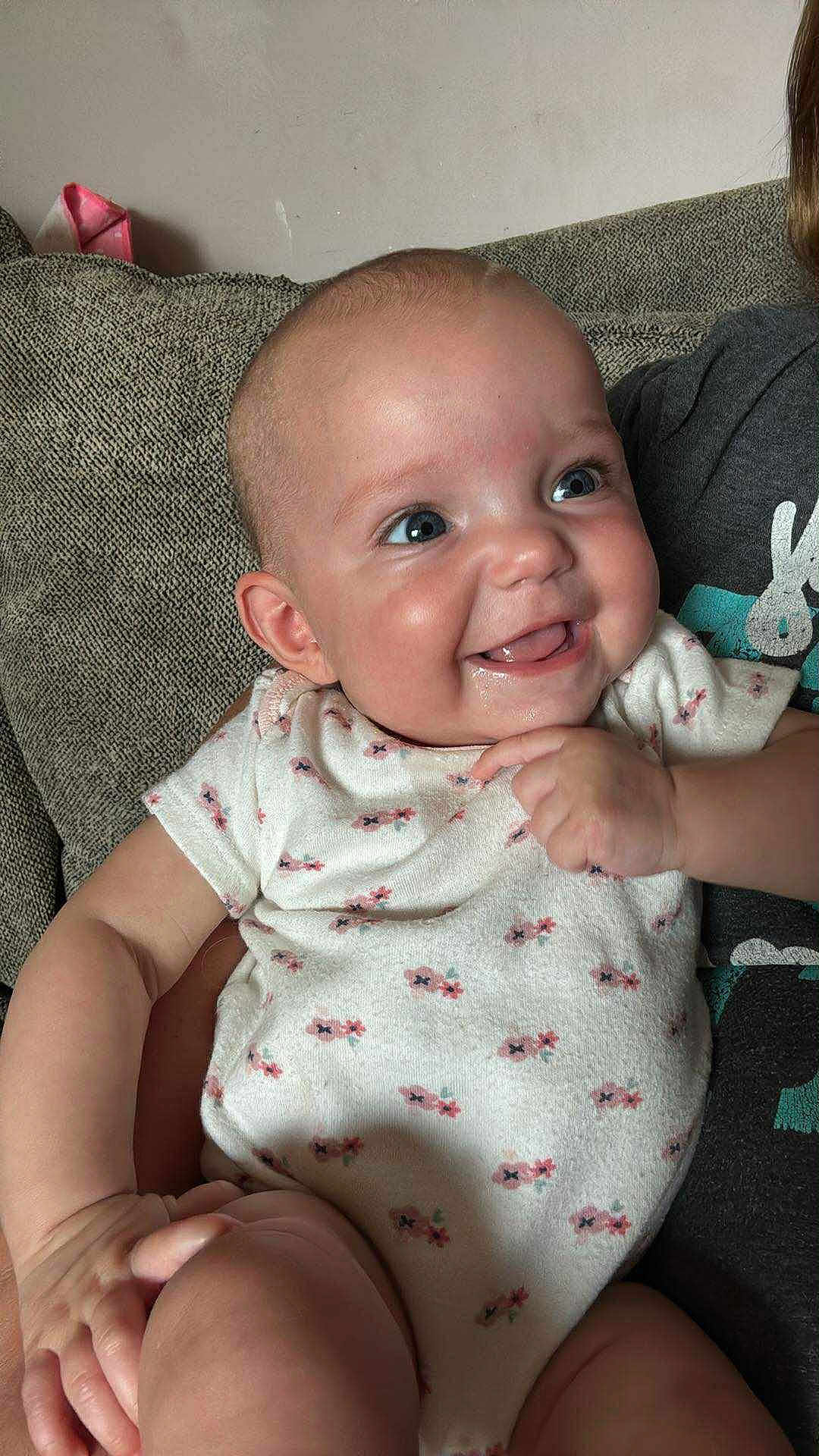 November Rain is registered to the contest to win money with this photo: baby, smiling, infant, onesie, couch, happy, child, person, skin, face, hand, blue_eyes, sitting, indoor, cute, expression, young, plush, comfort, joy