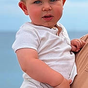 Eden a rejoint le concours — aidez-le/la à gagner de superbes lots ! adult_hand, baby, blonde_hair, blue_eyes, casual_clothing, child, cute, daylight, expression, face, hand, holding, ocean, outdoor, person, portrait, sky, summer, toddler, white_shirt