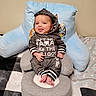 baby, infant, child, hoodie, clothing, sitting, smiling, tongue_out, face, eyes, hands, feet, baby_chair, pillow, blanket, indoor, wall, cute, cozy, portrait