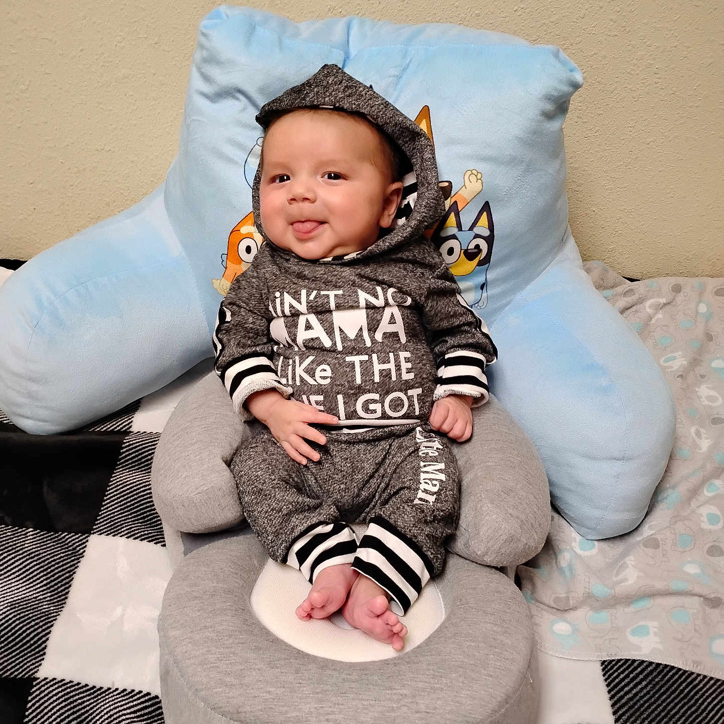 Amaziah is registered to the contest to win money with this photo: baby, infant, child, hoodie, clothing, sitting, smiling, tongue_out, face, eyes, hands, feet, baby_chair, pillow, blanket, indoor, wall, cute, cozy, portrait
