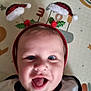 Léo participe au concours pour gagner de l'argent avec cette photo : baby, child, face, blue_eyes, headband, santa_hat, holiday, festive, smiling, open_mouth, clothing, bib, patterned_background, cute, infant, indoors, happy, person, portrait, closeup