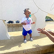 Allandrius joined the competition — help win amazing prizes! toddler, child, pacifier, blue_shorts, white_tshirt, sneakers, concrete, sculpture, outdoor, daylight, hands, person, shadow, urban, park, play, young_child, hair_buns, clothing, sidewalk