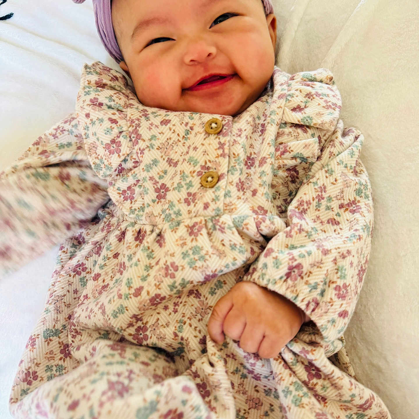 Mikaela joined the competition — help win amazing prizes! baby, bow, button, cheeks, child, clothing, cute, fabric, floral_dress, hand, happy, headband, infant, joy, lying_down, portrait, skin, smiling, soft_texture, white_background