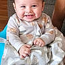 baby, child, infant, smiling, happy, portrait, sitting, onesie, blanket, couch, home, indoor, wooden_floor, brown_hair, face, hands, feet, patterned_clothing, family, cozy