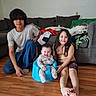 baby, children, family, siblings, smiling, happy, portrait, indoor, living_room, couch, blankets, pillows, wooden_floor, toy_airplane, blue_seat, long_hair, casual_clothing, sitting, infant, home