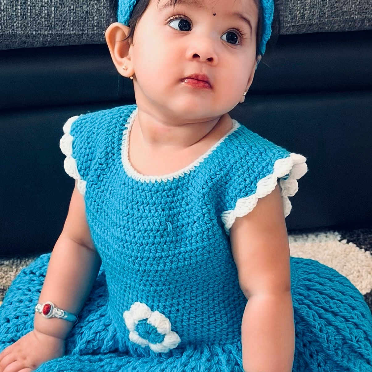 Edhaa is registered to the contest to win money with this photo: baby, child, girl, blue_dress, headband, crocheted_clothing, bracelets, indoor, carpet, cute, portrait, sitting, young_child, earrings, curious_expression, fashion, accessories, face, person, toddler