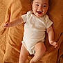 baby, infant, smiling, white_onesie, blanket, brown_blanket, lying_down, happy, cute, child, skin, face, head, barefoot, one_person, indoors, soft_texture, infant_clothing, small_child, joyful