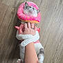 cat, pink_outfit, donut_collar, hugging, person_arm, wooden_floor, pet, cute, playful, domestic_animal, white_fur, gray_patches, paws, tattoo, clothing, animal_collar, indoor, affection, pet_costume, funny