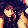 Evie joined the competition — help win amazing prizes! woman, cat, indoor, black_clothing, lace, witch_hat, fluffy_cat, siamese_cat, portrait, red_lipstick, long_hair, pet, cozy, face, holding, feline, closeup, seated, warm_lighting, smile