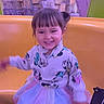 child, girl, smiling, jacket, tutu_skirt, shoes, yellow_seat, amusement_ride, rock_background, indoor, playful, happy, person, casual_clothing, short_hair, colorful, portrait, fun, cute, young