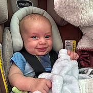 Ryker is registered to the contest to win money with this photo: baby, car_seat, blanket, smile, infant, child, blue_shirt, safety_harness, cozy, cute, face, head_support, soft_texture, indoors, happy, young_child, seat, child_safety, toddler, expression