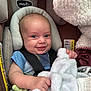 baby, car_seat, blanket, smile, infant, child, blue_shirt, safety_harness, cozy, cute, face, head_support, soft_texture, indoors, happy, young_child, seat, child_safety, toddler, expression