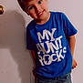 blue_tshirt, boy, casual_clothing, child, cute, denim_shorts, door, expression, happy, indoor, light_skin, person, playful, portrait, shadow, short_hair, smiling, standing, text_on_clothing, young