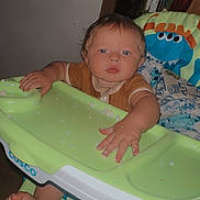 Xander is registered to the contest to win money with this photo: baby, blanket, blue_eyes, brown_hair, child, clothing, curious, expression, face, food, foot, furniture, green, hand, high_chair, indoor, kitchen, plastic, seated, toy_design