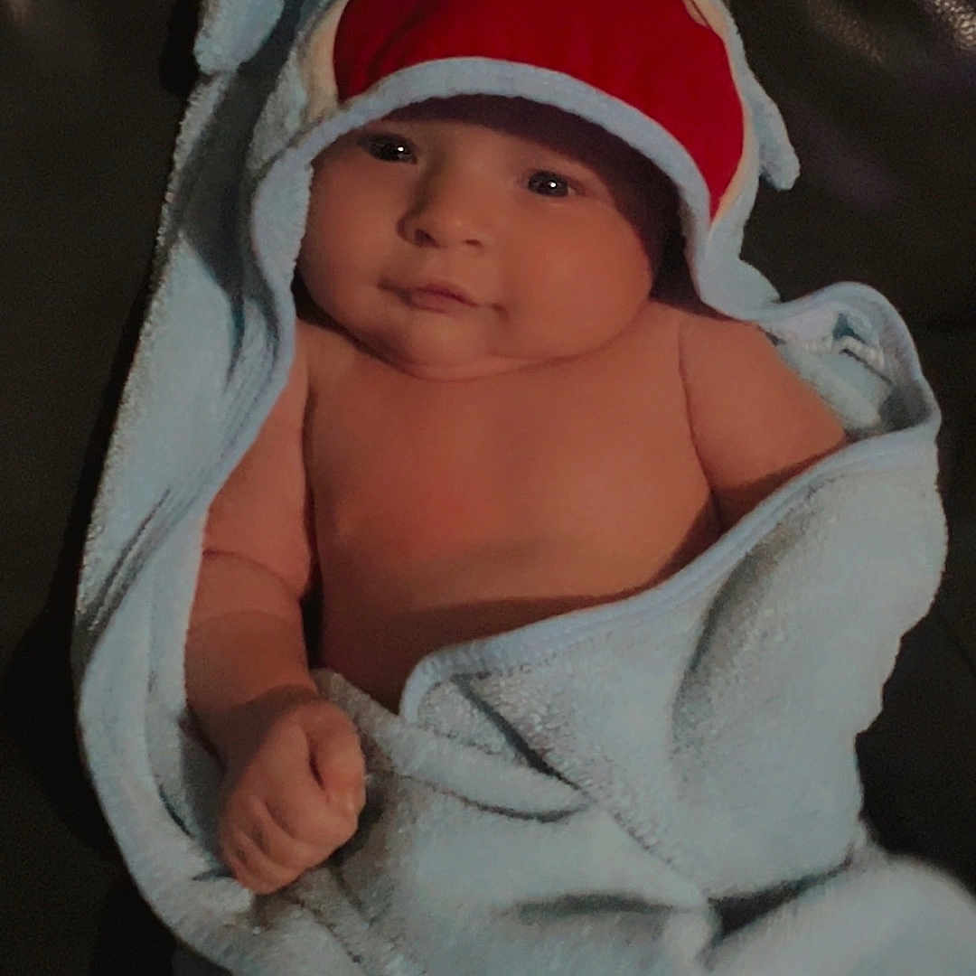 Xander is registered to the contest to win money with this photo: adorable, baby, blanket, blue, child, clothing, cute, face, hand, indoors, infant, leather_couch, portrait, shark_hood, skin, smile, soft, towel, wrapped, young