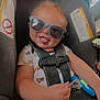 Xander is registered to the contest to win money with this photo: baby, car_seat, casual, child, cute, happy, indoor, infant, monkey_print, onesie, person, playful, safety, seat, seatbelt, smiling, sunglasses, toddler, tongue_out, toy