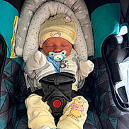 Cashton is registered to the contest to win money with this photo: baby, infant, newborn, car_seat, pacifier, hat, mittens, buckle, safety_harness, booties, sleeping, cute, cozy, padded_headrest, patterned_fabric, cartoon_print, straps, seat_pad, portrait, soft_lighting