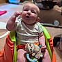 baby, infant, child, plush_toy, sloth_toy, baby_seat, orange, green, carpet, indoor, curious, expression, raised_arm, clothing, onesie, toy, soft_toy, seat_belt, floor, home
