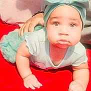 Majesty is registered to the contest to win money with this photo: baby, infant, child, headband, bow, onesie, mint_clothing, red_blanket, crawling, chubby_cheeks, big_eyes, closeup, portrait, indoor, hand, adult_hand, bracelet, cute, skin, toddler