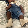 Jaevion is registered to the contest to win money with this photo: baby, infant, child, portrait, lying_down, bed, checkered_blanket, blue_hat, denim_overalls, striped_shirt, booties, clothing, fashion, dark_skin, indoor, cozy, sitting, looking_up, bedroom, photography