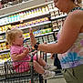 toddler, child, adult, shopping_cart, grocery_store, aisle, dairy_products, high_five, woman, pacifier, casual_clothing, footwear, socks, blonde_hair, interaction, shopping, retail, supermarket, parent, bonding