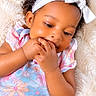 baby, blanket, bow, child, close_up, colorful_clothing, curly_hair, cute, face, floral_dress, hand_to_mouth, hands, headband, indoor, infant, lying_down, photography, portrait, smiling, soft_texture