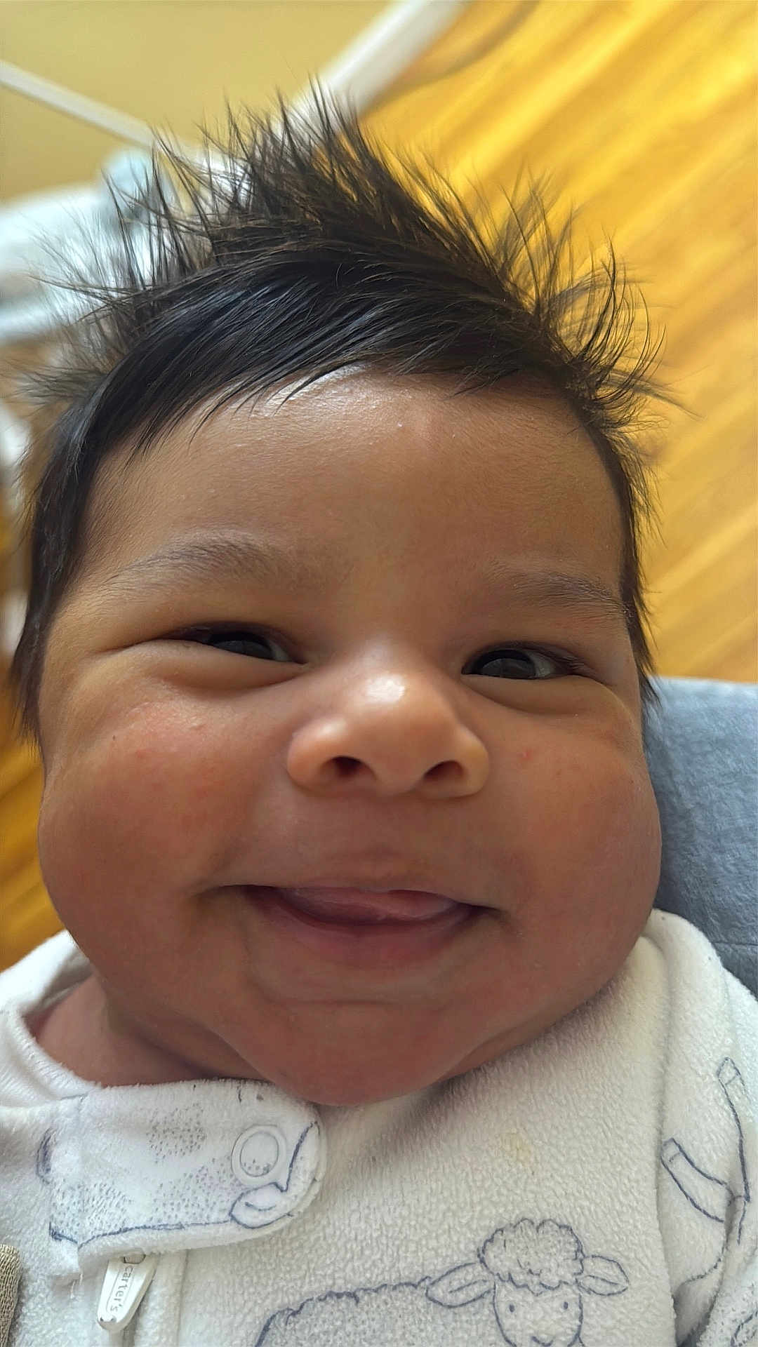 Jussuf is registered to the contest to win money with this photo: baby, smiling, close_up, face, hair, spiky_hair, onesie, white_clothing, infant, cute, happy, child, portrait, skin, indoors, person, young, expression, cheeks, button