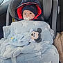 baby, car_seat, blanket, pacifier, hat, jacket, plush_toy, mickey_mouse, child, indoor, seatbelt, car_interior, window, reflection, cozy, warm_clothing, child_protection, car_trip, infant, cute
