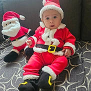 Aylan participe au concours pour gagner de l'argent avec cette photo : baby, santa_suit, plush_toy, stuffed_santa, red_clothing, white_fur_trim, black_belt, black_boots, hat, holiday, christmas, cute, child, indoor, couch, patterned_blanket, festive, smiling, portrait, infant