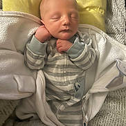 William is registered to the contest to win money with this photo: baby, newborn, sleeping, blanket, pajamas, striped_clothing, yellow_pillow, cozy, infant, soft_texture, hands, face, peaceful, resting, indoors, closeup, cute, child, person, wrapped